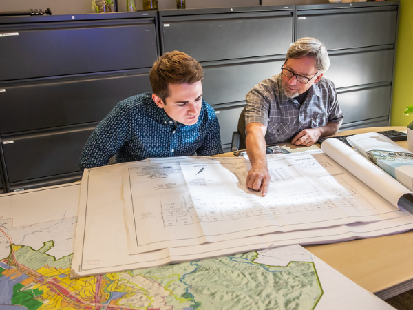 Image of two individuals looking over project plans spread across a table.