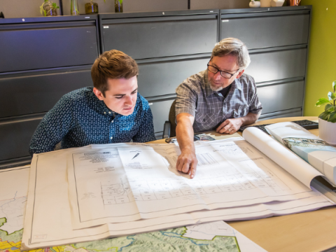 Two people sitting at a table and looking through a planset.